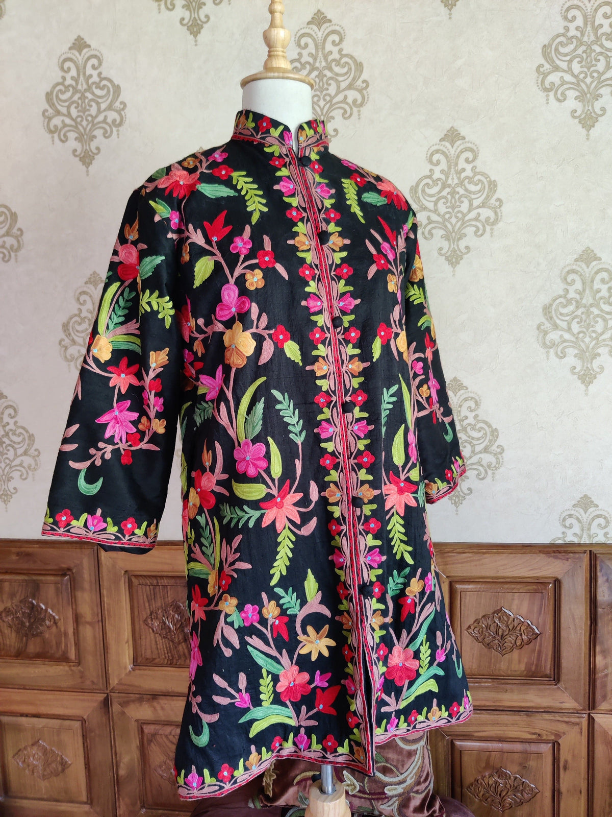 Angled full front of a black jacket with multicoloured Aari floral vines, a stand collar and wide embroidered sleeves