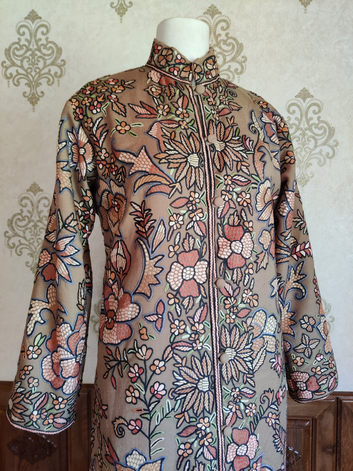 Upper front of the beige wool jacket, showing its band collar and pastel floral Hand Aari embroidery