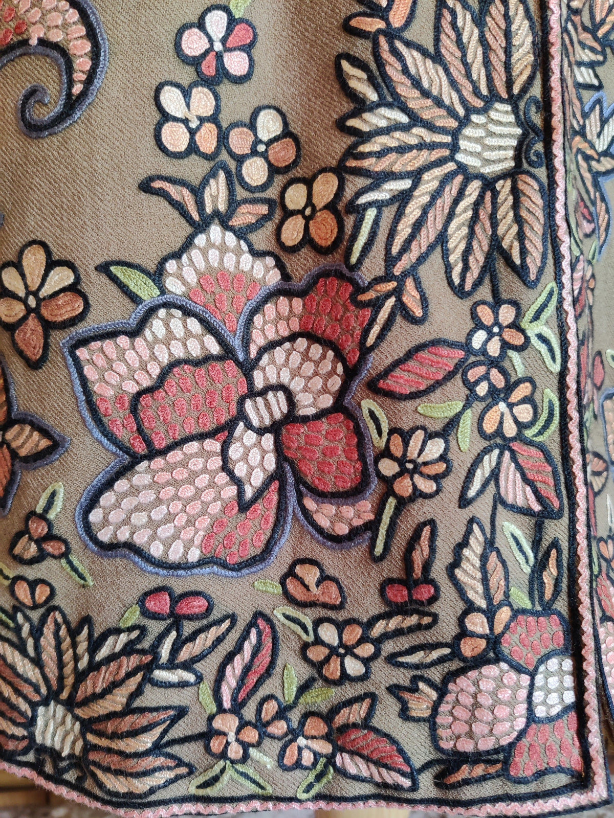 Lower-front detail of the beige wool Hand Aari jacket, with pink and cream flowers beside the embroidered hem