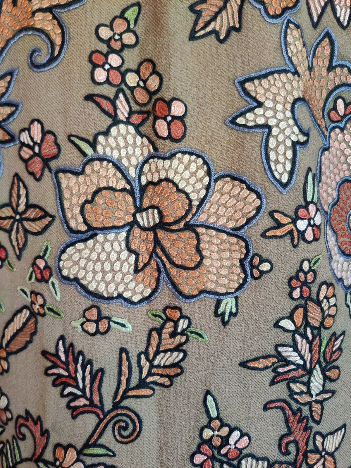 Close-up of peach and cream Hand Aari flowers with dark outlines and green leaves on the beige wool jacket