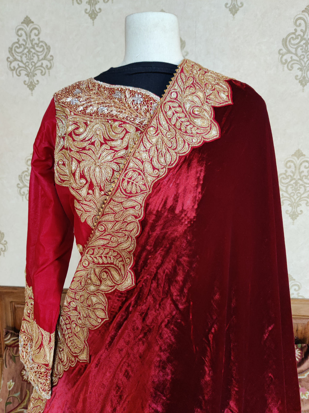 Shoulder detail of a maroon velvet dupatta crossing the red embroidered top, with a scalloped golden floral and paisley border