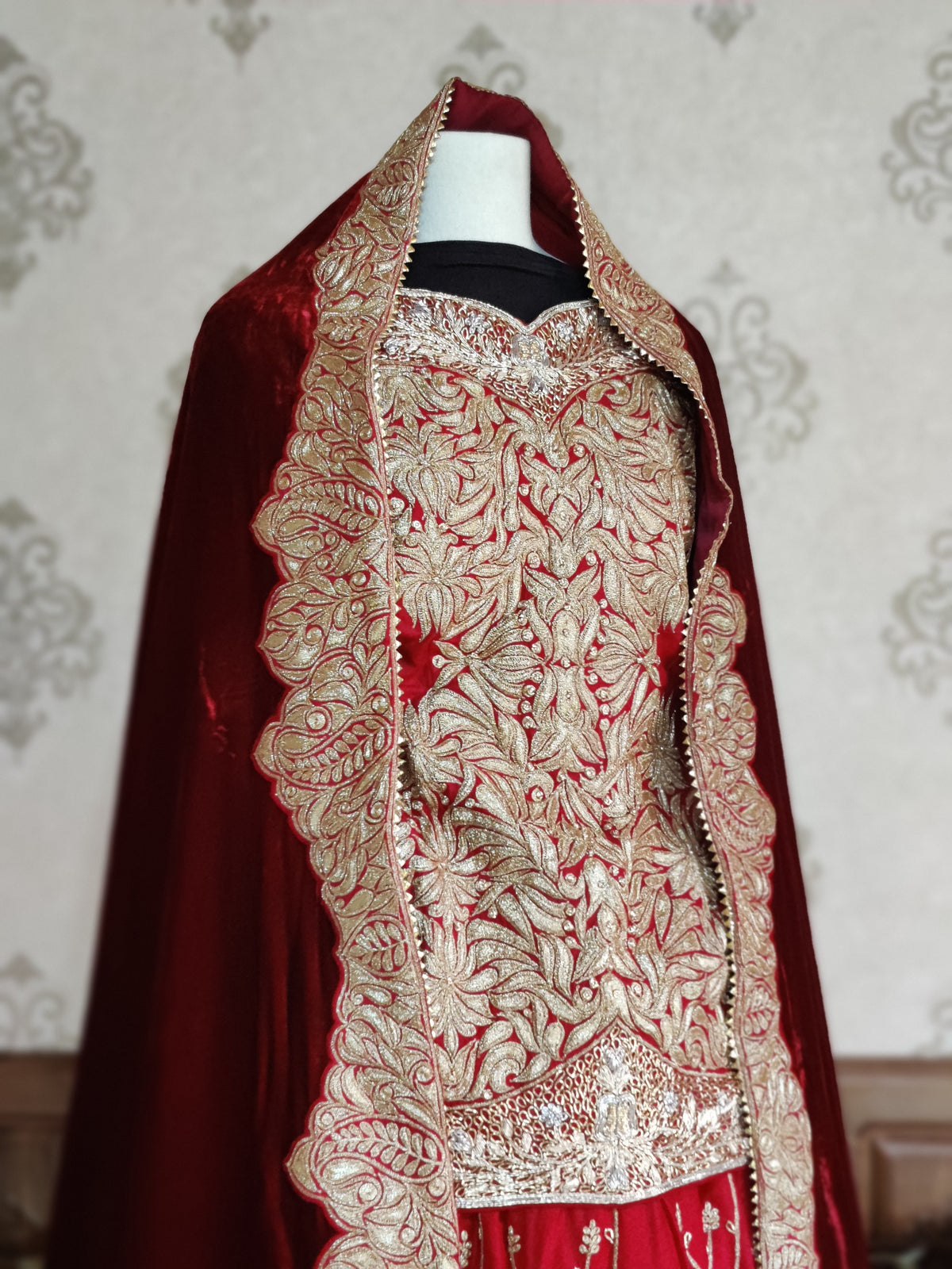 Angled close-up of the red top’s dense golden Tilla embroidery beneath the maroon dupatta draped over the mannequin’s head