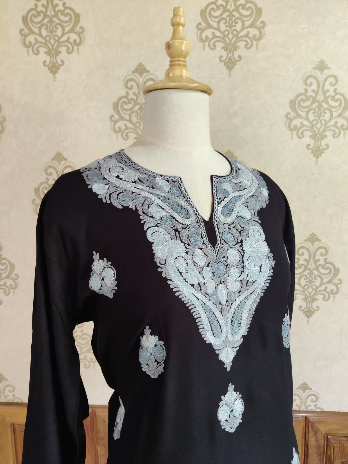 Angled upper view of the black kurti, showing its silver-grey Aari neckline panel and scattered floral motifs.