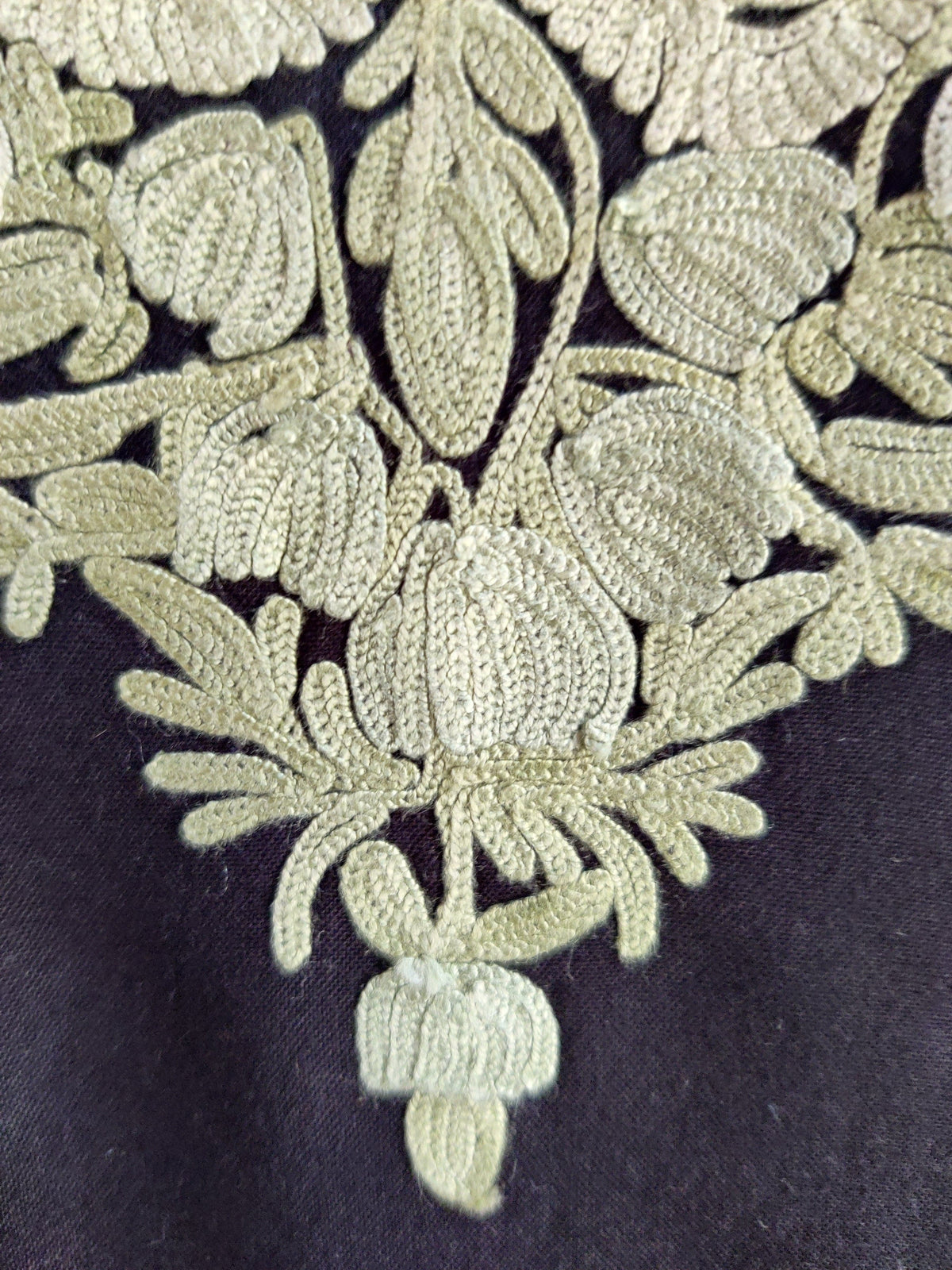 Macro detail of mint-green Aari flowers and leaves forming the pointed base of the black kurti’s embroidered neckline panel.
