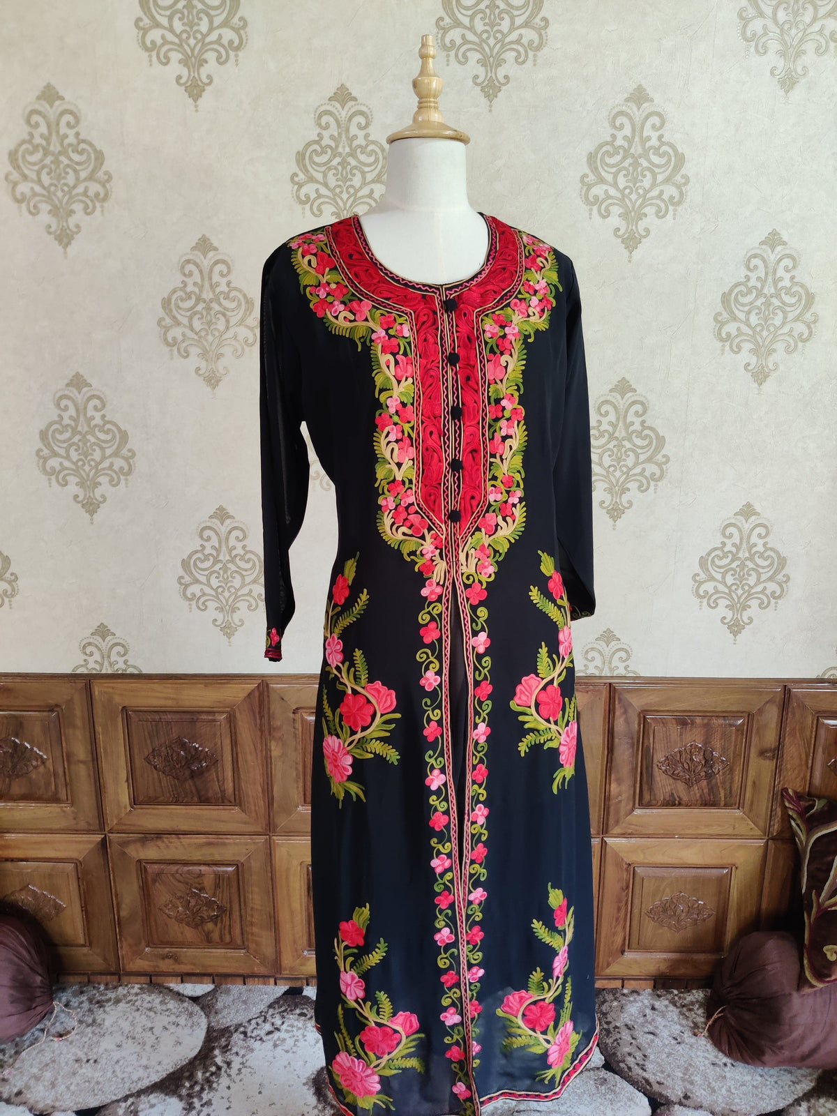 Full front of a black kaftan on a mannequin, with red and pink Aari flowers along the neckline, centre and lower sides