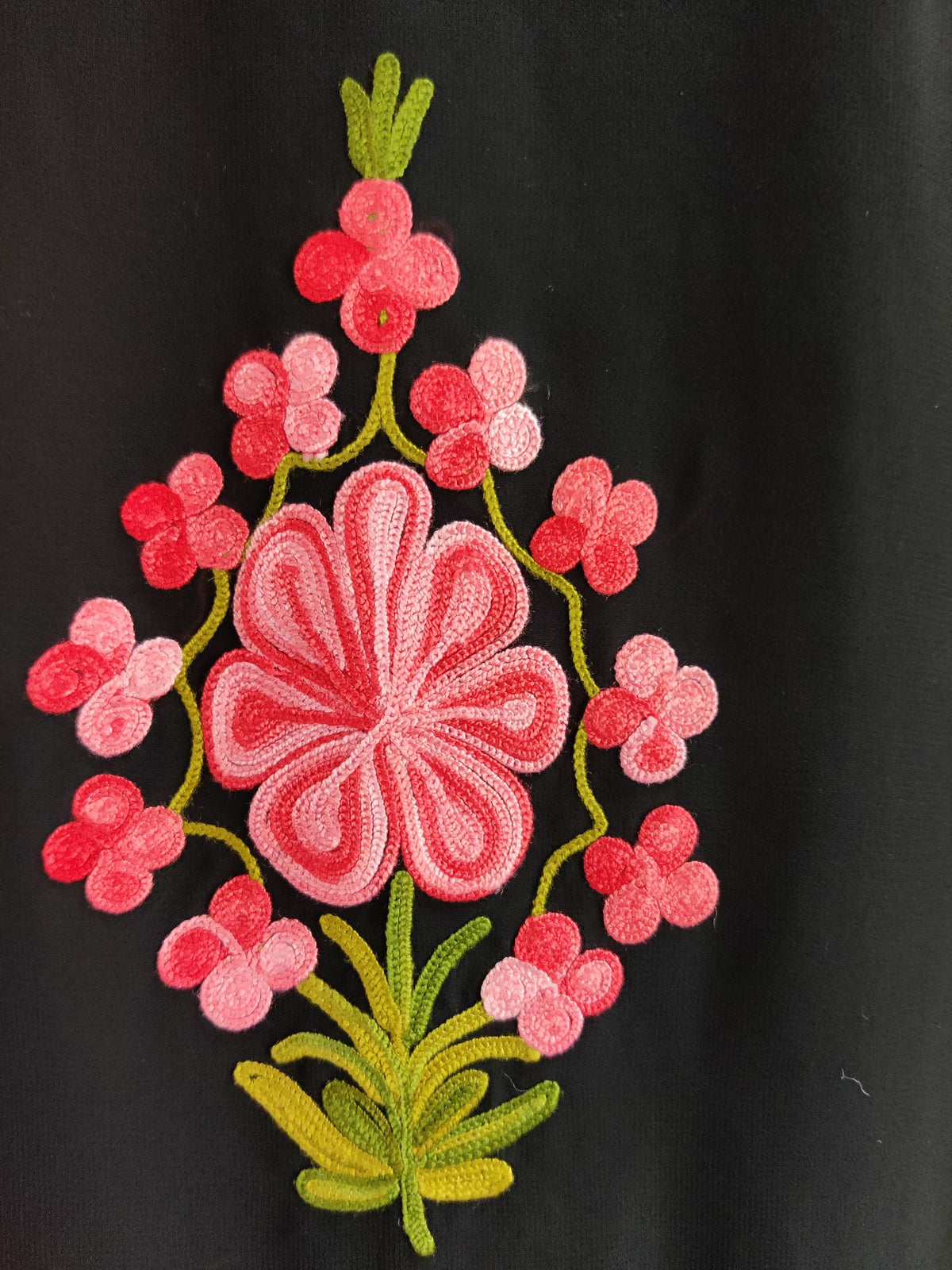 Close-up of a pink Aari flower surrounded by small red and pink blossoms on green stems against black fabric