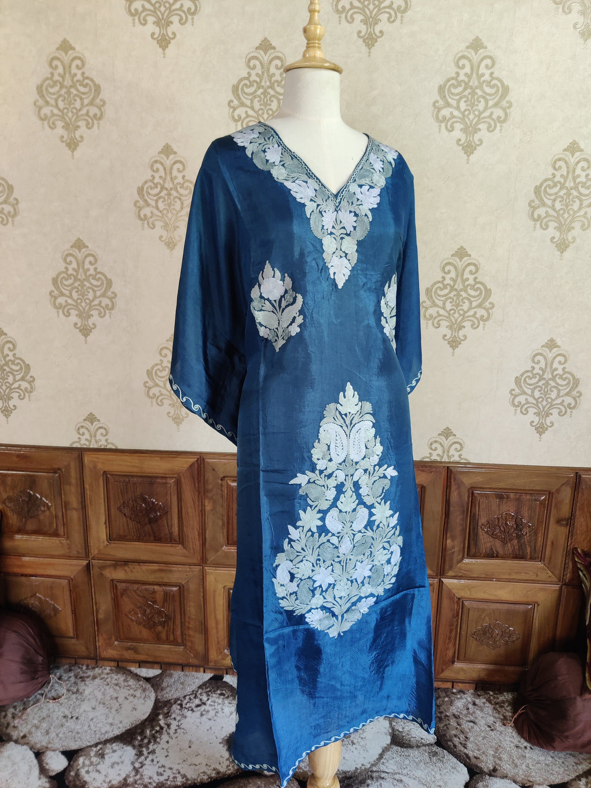 Full-length ocean-blue kaftan on a mannequin, with white floral motifs, a large lower paisley arrangement and wide draped sleeves.