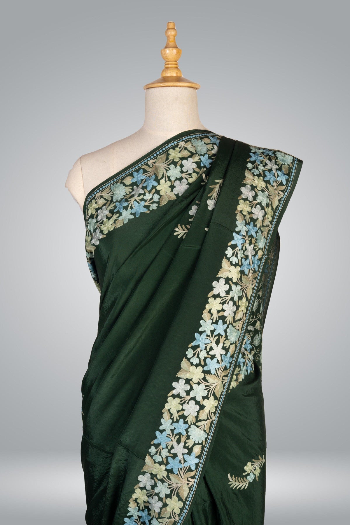 Upper drape of a green crepe saree with cream and pale blue Aari flowers along the shoulder and diagonal border
