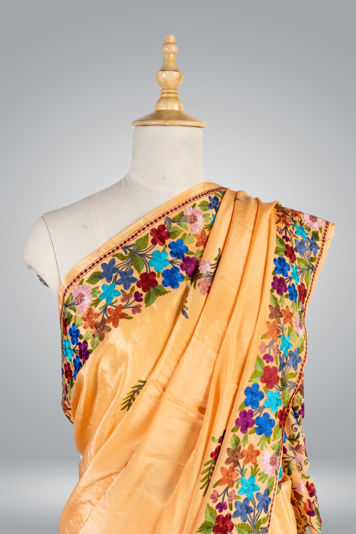 Upper draped view of a light-orange crepe saree with a broad multicoloured floral border across the shoulder.