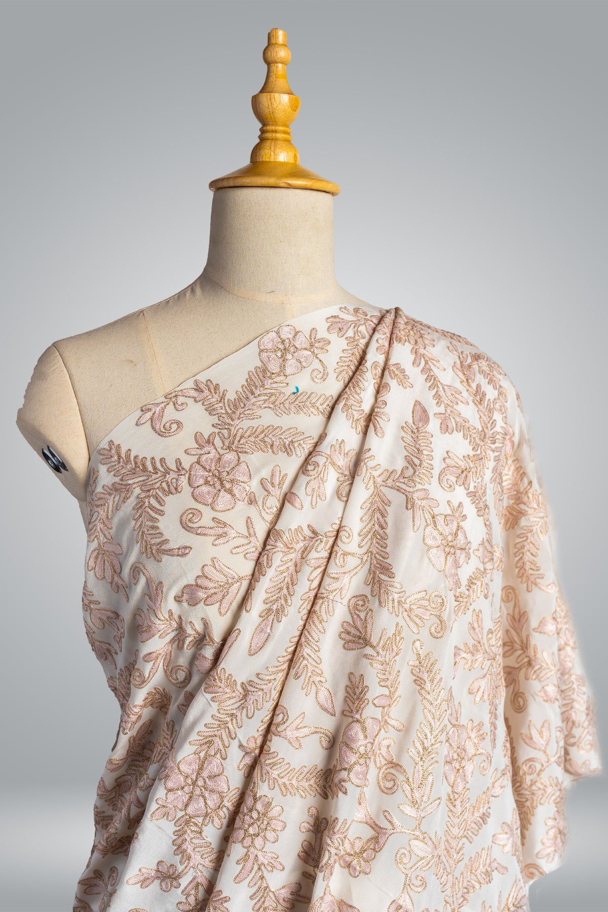 Upper drape of a white crepe sari over a mannequin, with pale beige-pink Aari floral embroidery and gold Zari outlines