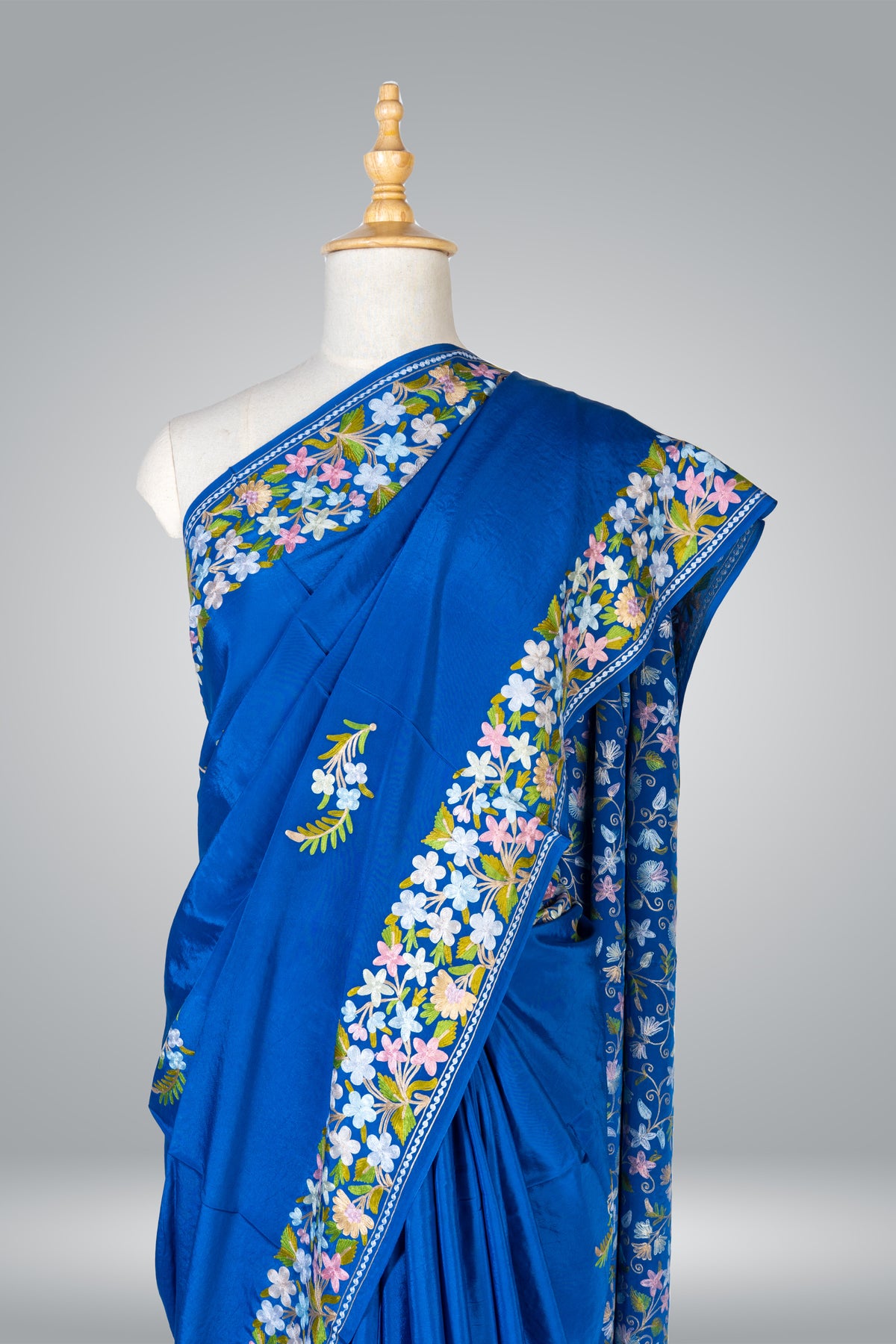 Upper drape of a royal blue crepe sari showing a pastel Aari floral border over the shoulder and a small flower sprig