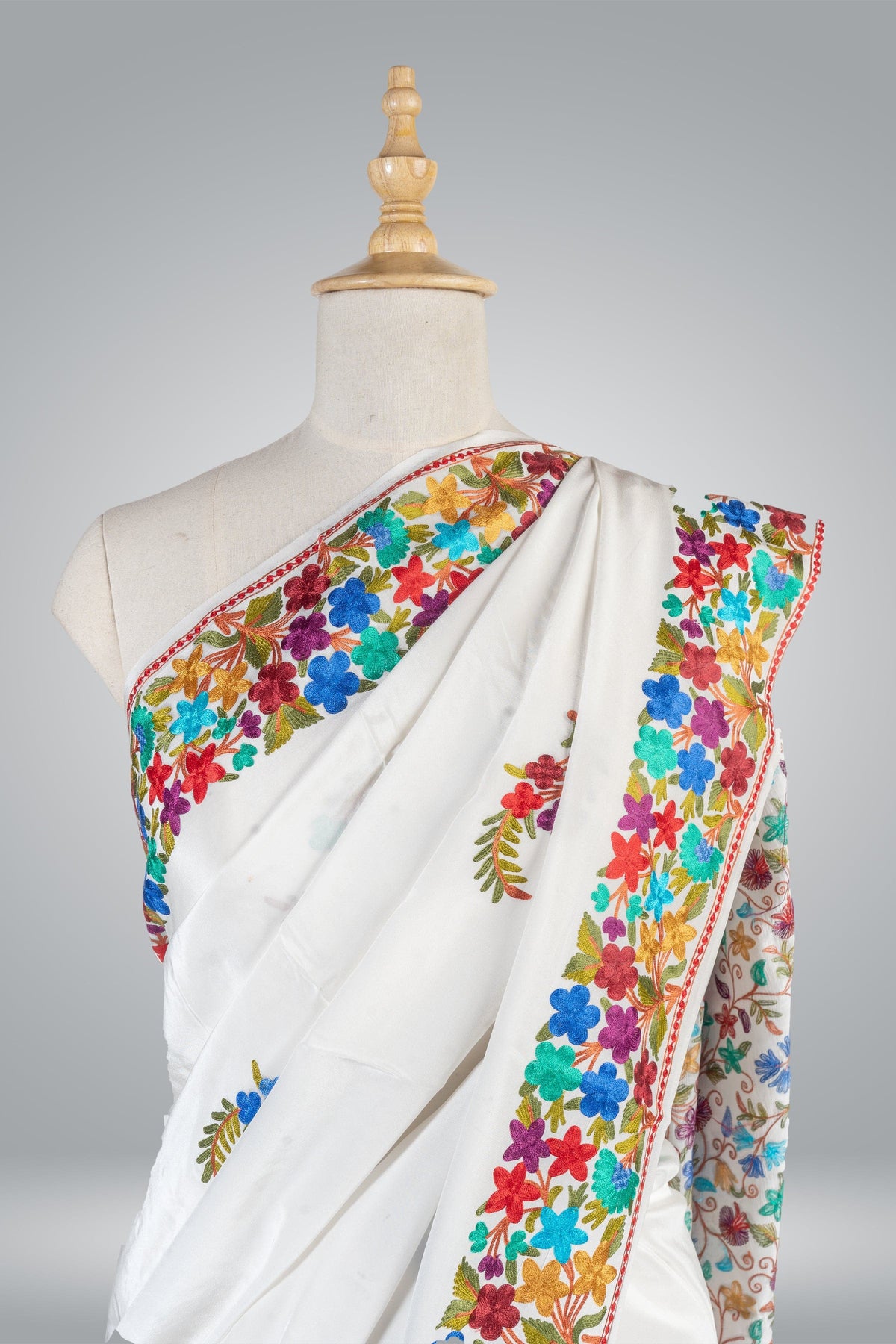 Upper drape of a white crepe saree with bright blue, red, purple and turquoise Aari flowers along the border