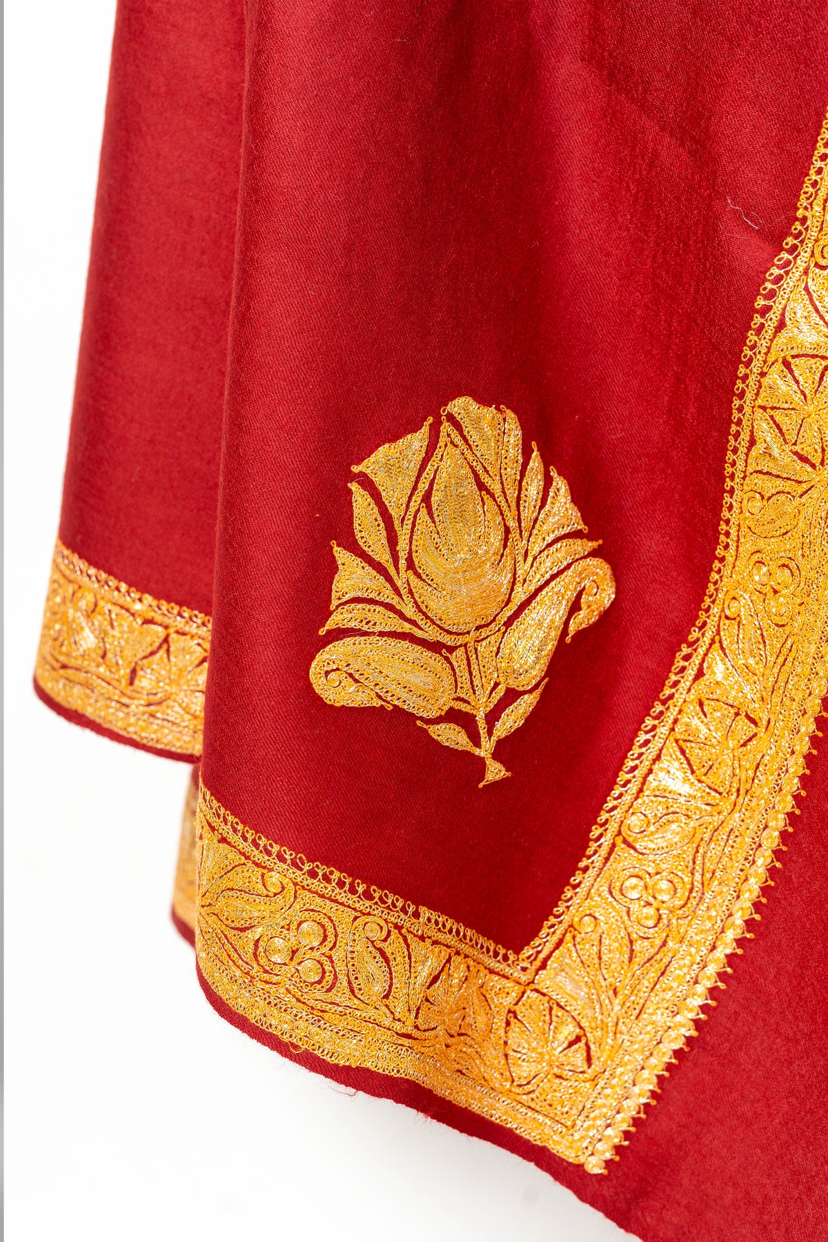 Draped corner of the red Merino wool shawl, showing a large gold Tilla flower above the floral border.