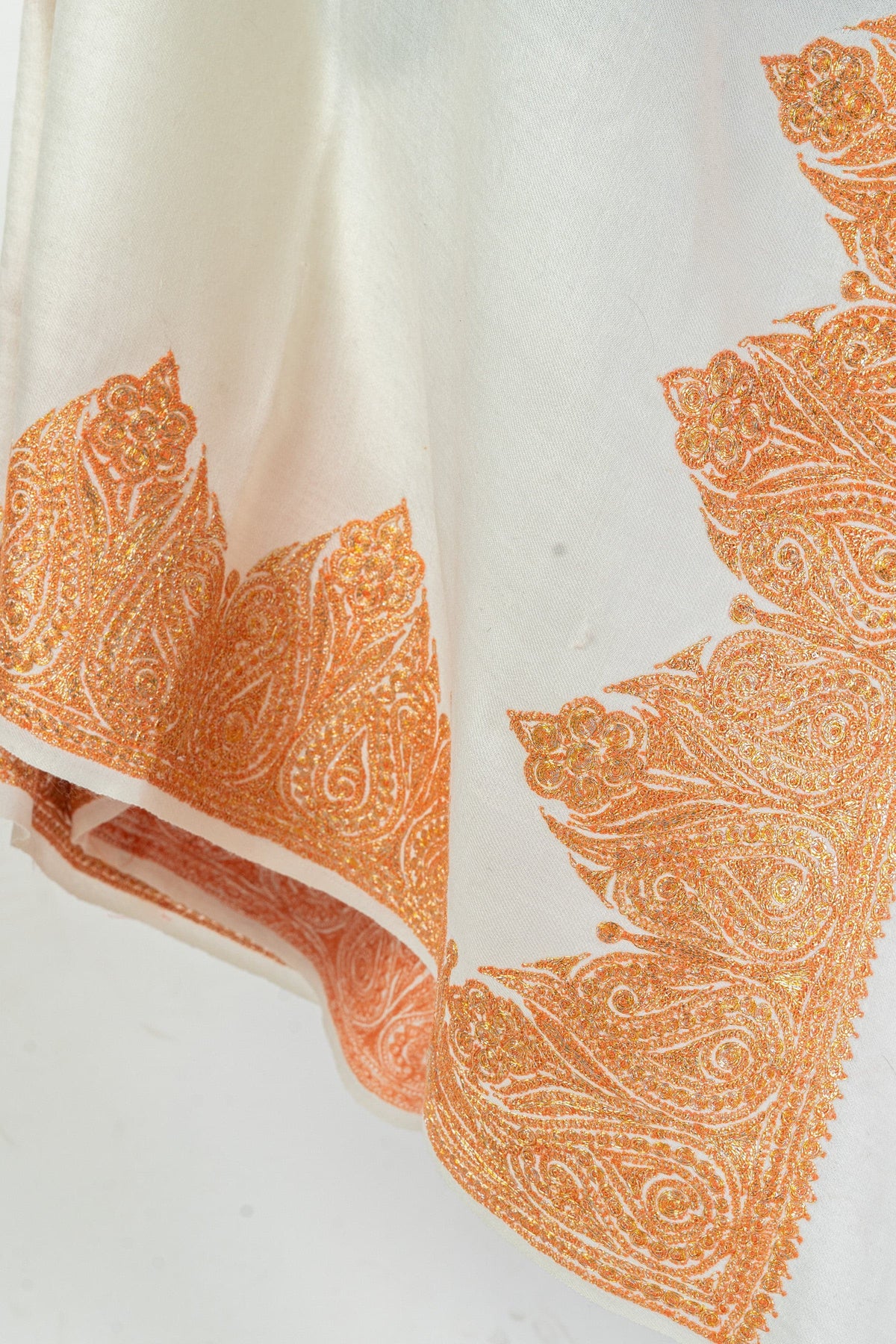 Folded lower edge of a white Merino wool shawl with orange-gold paisley Tilla embroidery
