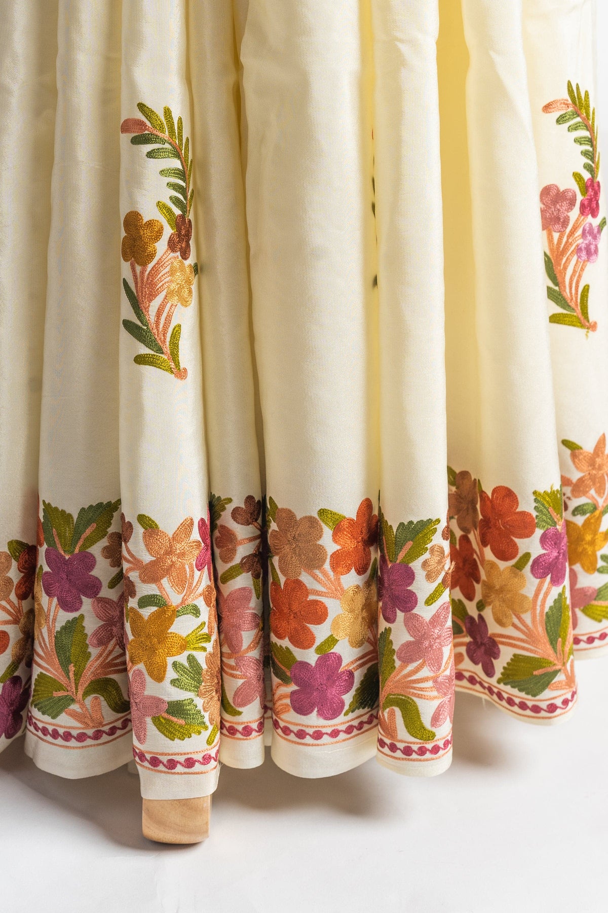 Lower pleats of the cream saree with scattered floral sprigs and a broad multicoloured embroidered hem border.