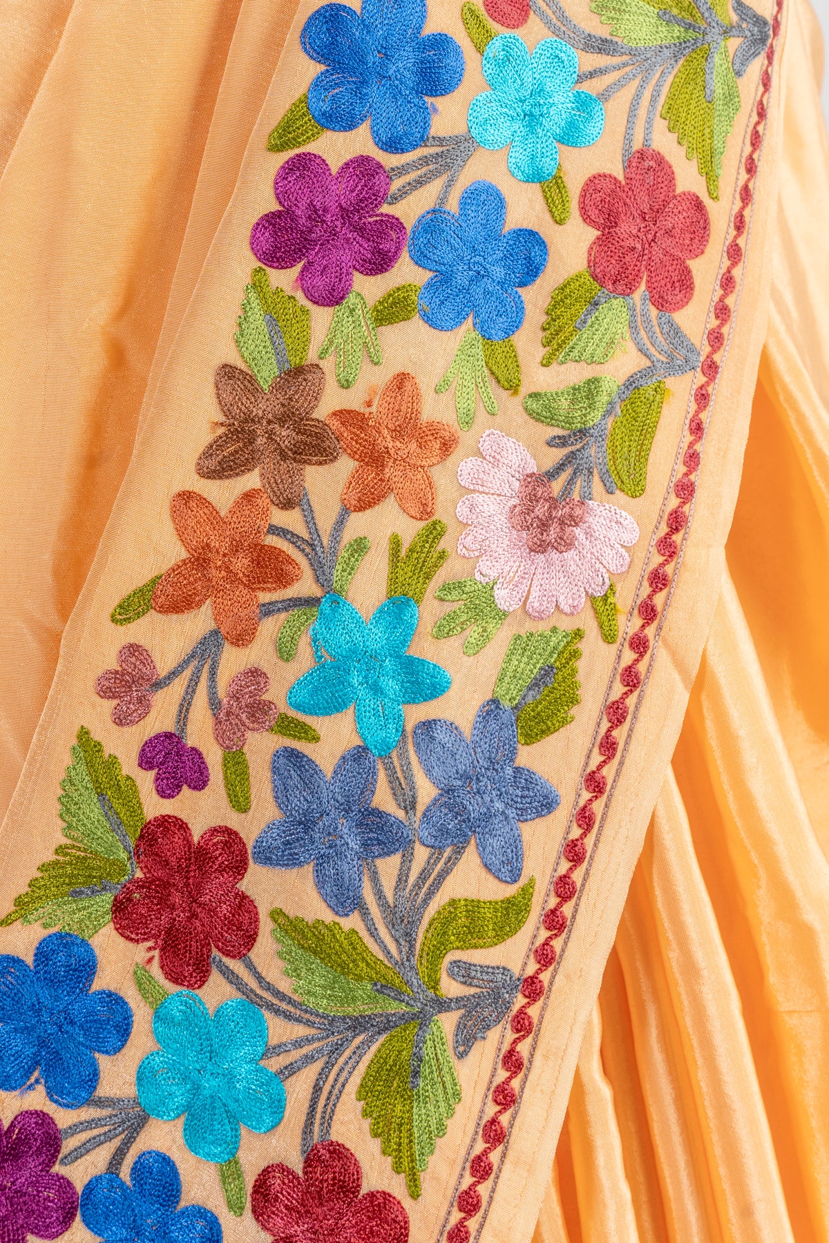 Close-up of the light-orange saree border with blue, turquoise, purple and coral flowers, green leaves and a narrow pink edge.