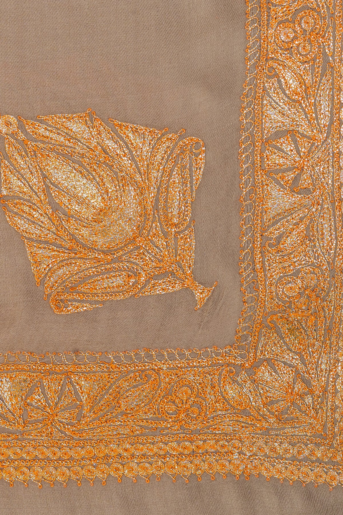 Close-up of a golden-orange Tilla leaf motif beside the embroidered corner border on a beige shawl