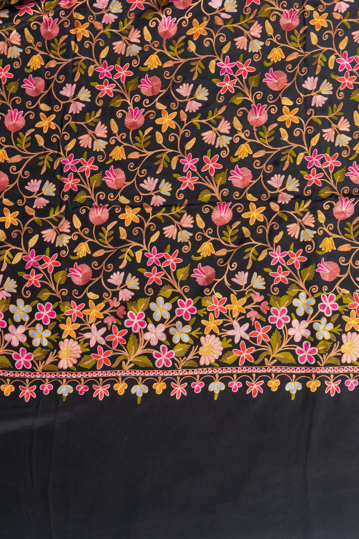 Flat detail of the black crepe saree with colourful Aari floral vines and a denser flower border above a plain black end.