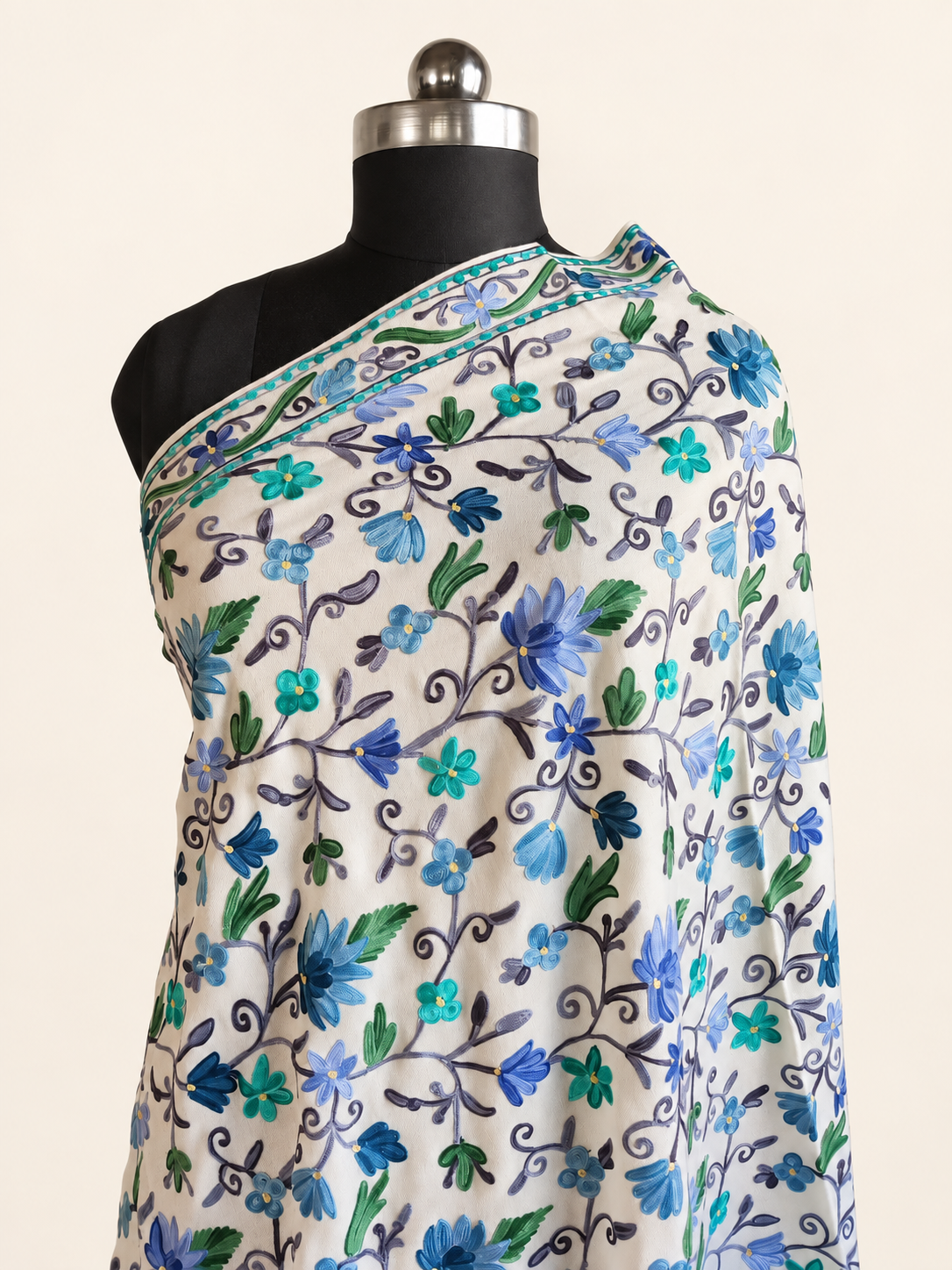 White fine Merino wool shawl with blue, turquoise and green Aari floral embroidery, close draped view on an ivory studio background