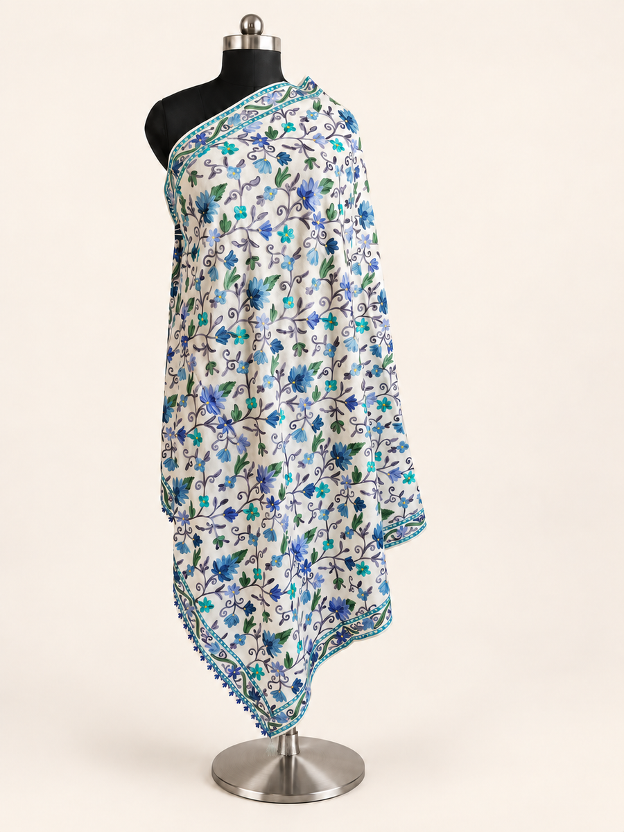 White fine Merino wool shawl with blue, turquoise and green Aari floral embroidery, full draped view on an ivory studio background