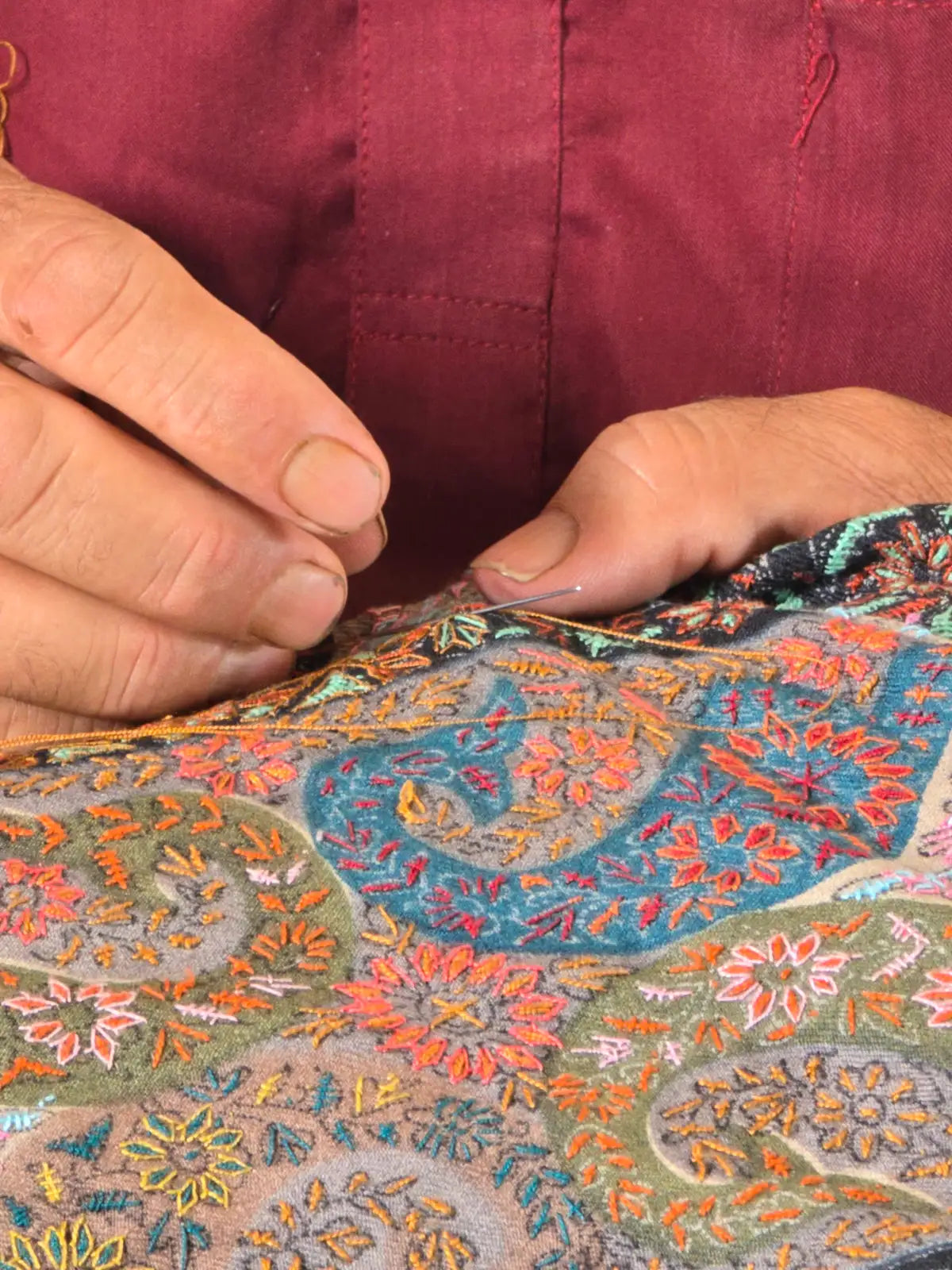 An artisan’s hands guiding a fine needle through colourful Sozni embroidery.
