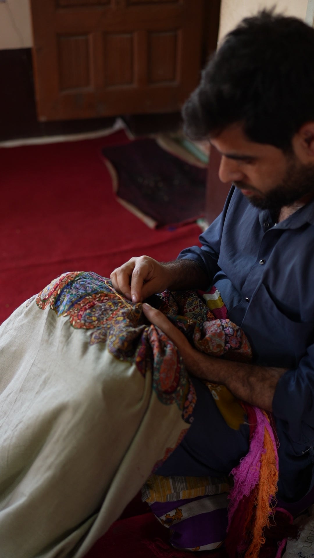 An artisan in a blue shirt working fine needle embroidery on a shawl