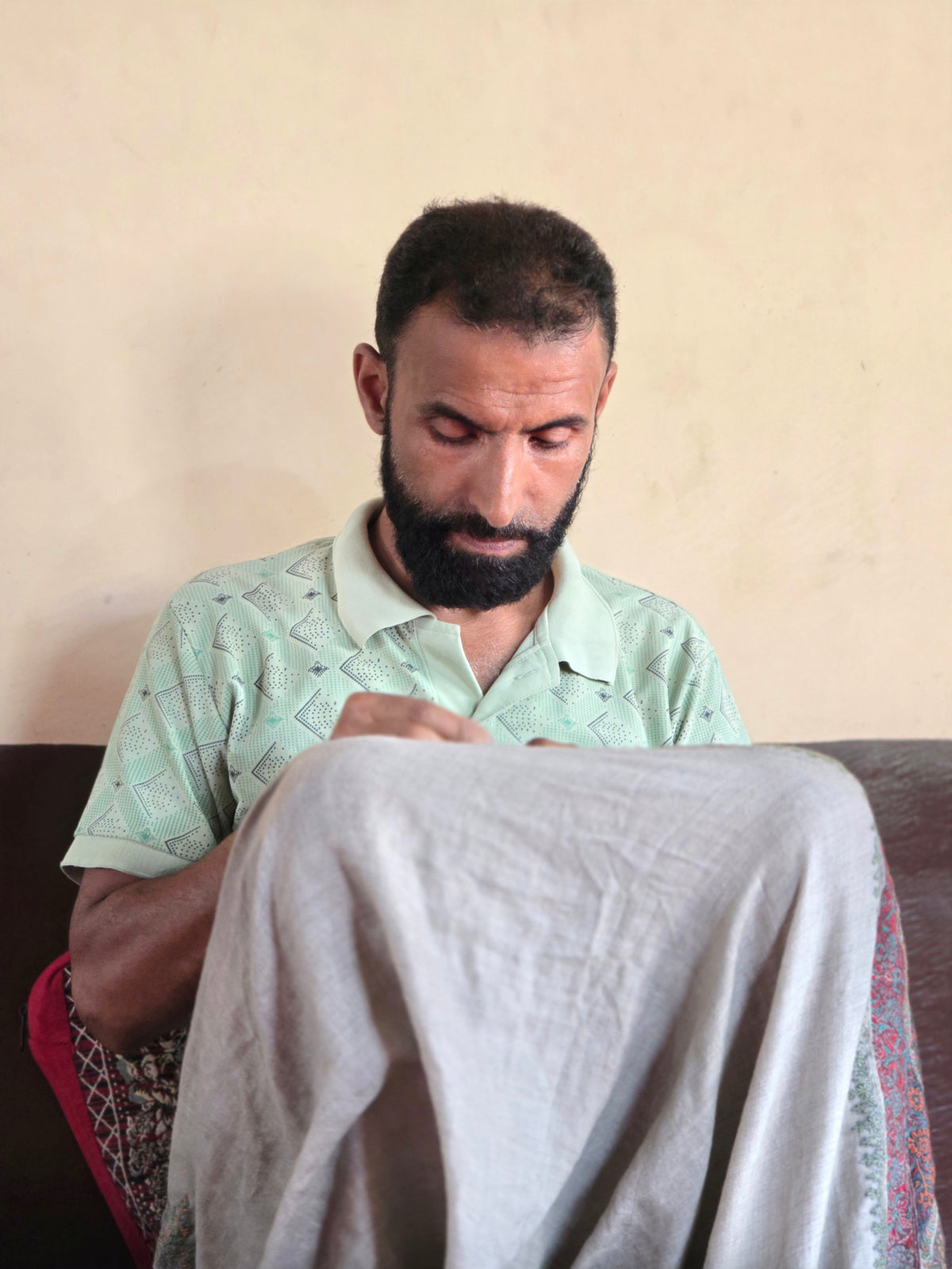 An artisan in a pale green shirt embroidering a light shawl by hand