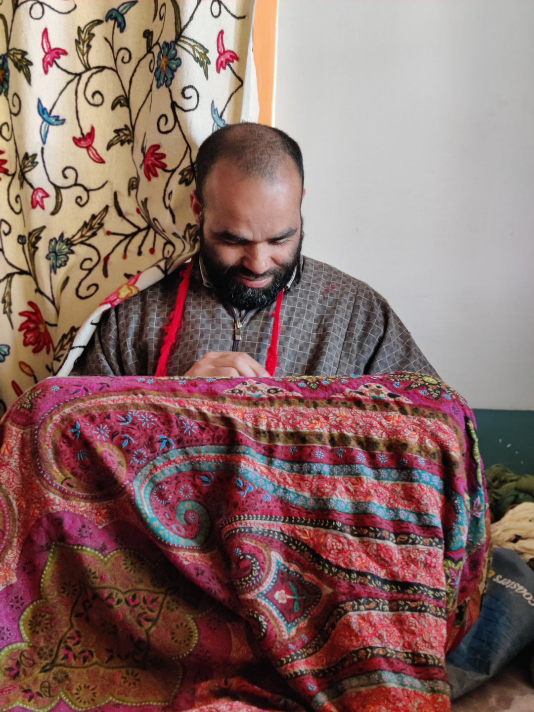 A Kashmiri artisan working by hand on a richly patterned pink shawl in the workshop