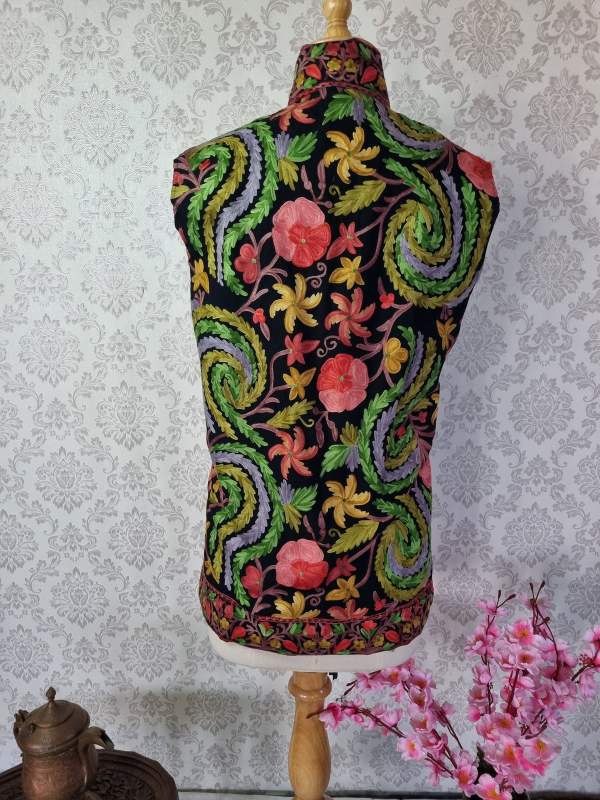 Back of a black sleeveless jacket, covered with green and lavender Aari paisleys, red flowers and smaller yellow floral motifs.