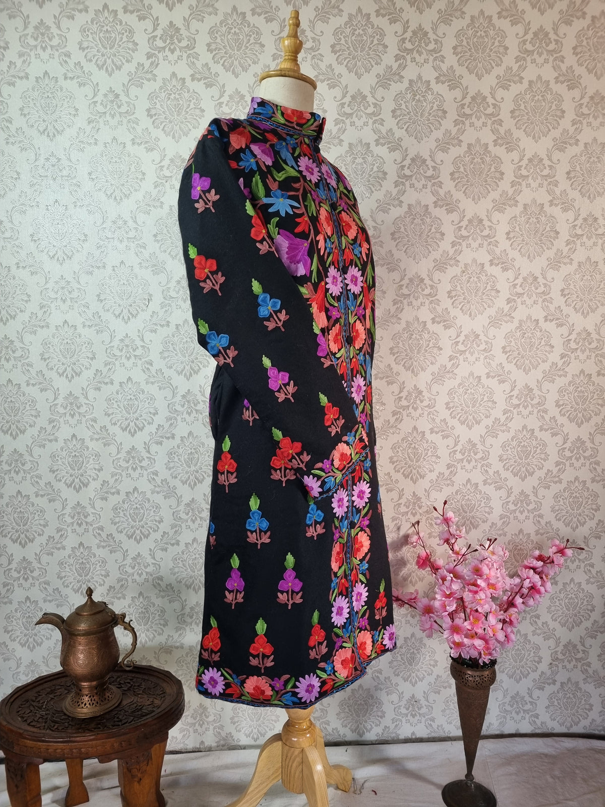 Three-quarter view of a black jacket showing bright floral embroidery across the chest and small scattered motifs down the side.