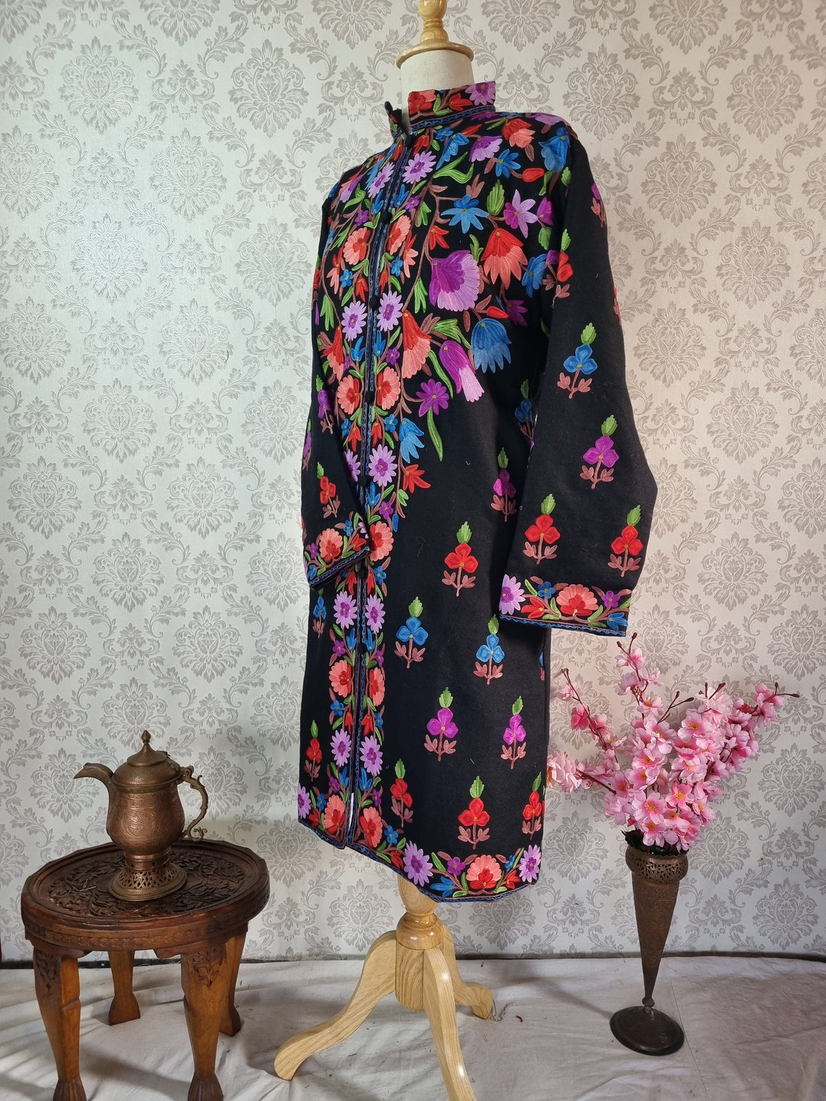 Angled full view of the black jacket with colourful floral front panels, small scattered flowers and a patterned cuff and hem.
