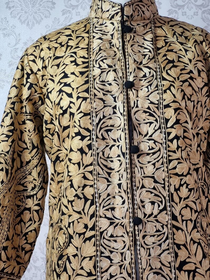 Close-up of the black jacket's stand collar and buttoned front, with dense beige Aari leafy vines and a floral placket border.