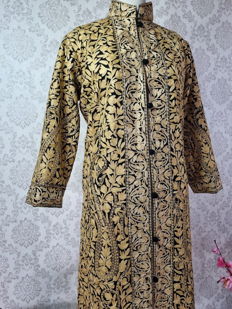Front of a black long jacket with sleeves hanging down, showing beige Aari paisleys and leafy vines across the body and sleeves.