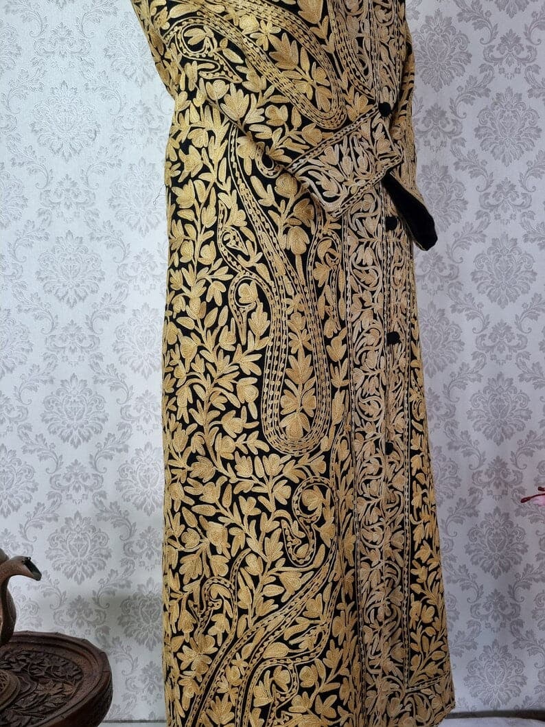 Side-front detail of a black long jacket, showing large beige Aari paisleys, dense leafy embroidery and a crossed cuff.