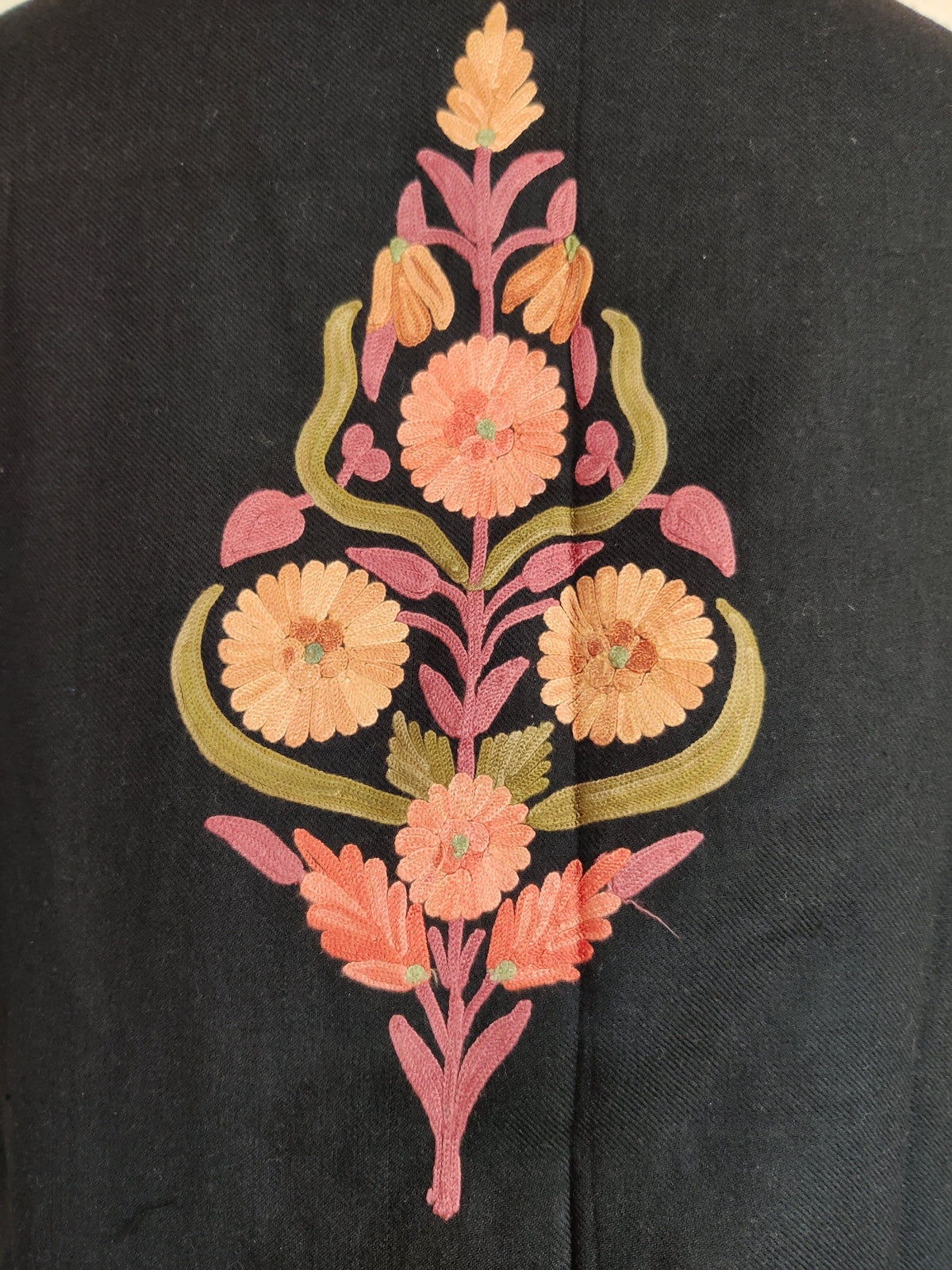 Close-up of the black jacket's back motif, with peach Aari flowers, pink branching stems and curved olive-green leaves.
