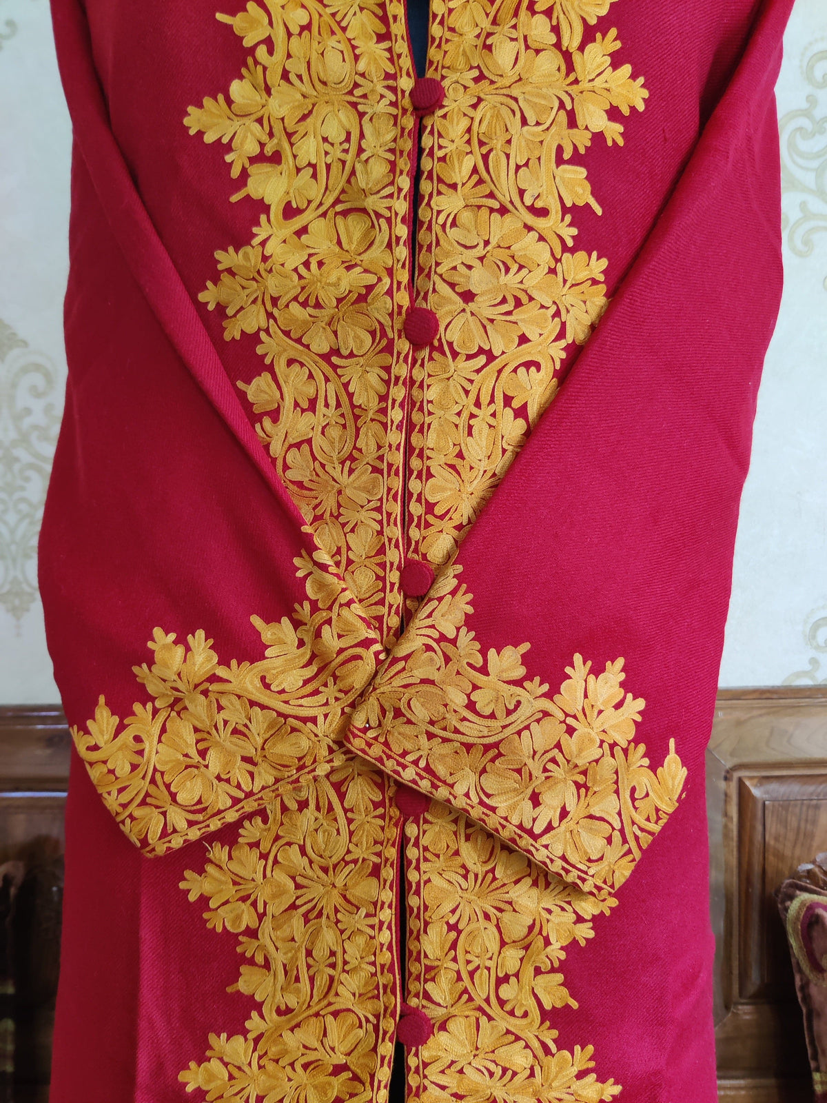 Close-up of golden-yellow Aari floral borders and crossed embroidered cuffs on the maroon jacket.