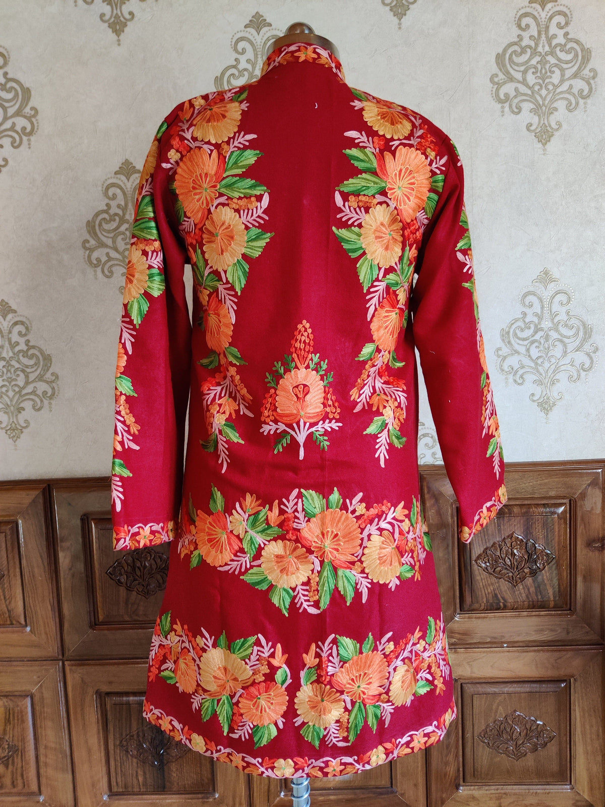 Back of a maroon jacket with orange floral trails at the shoulders, a small central motif and broad flower bands near the hem.