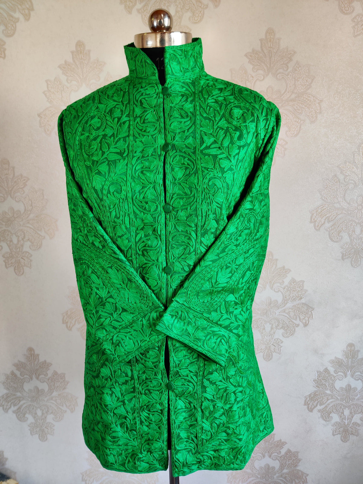 Full front of a green jacket with crossed sleeves, covered buttons and all-over tonal Aari flowers and leaves