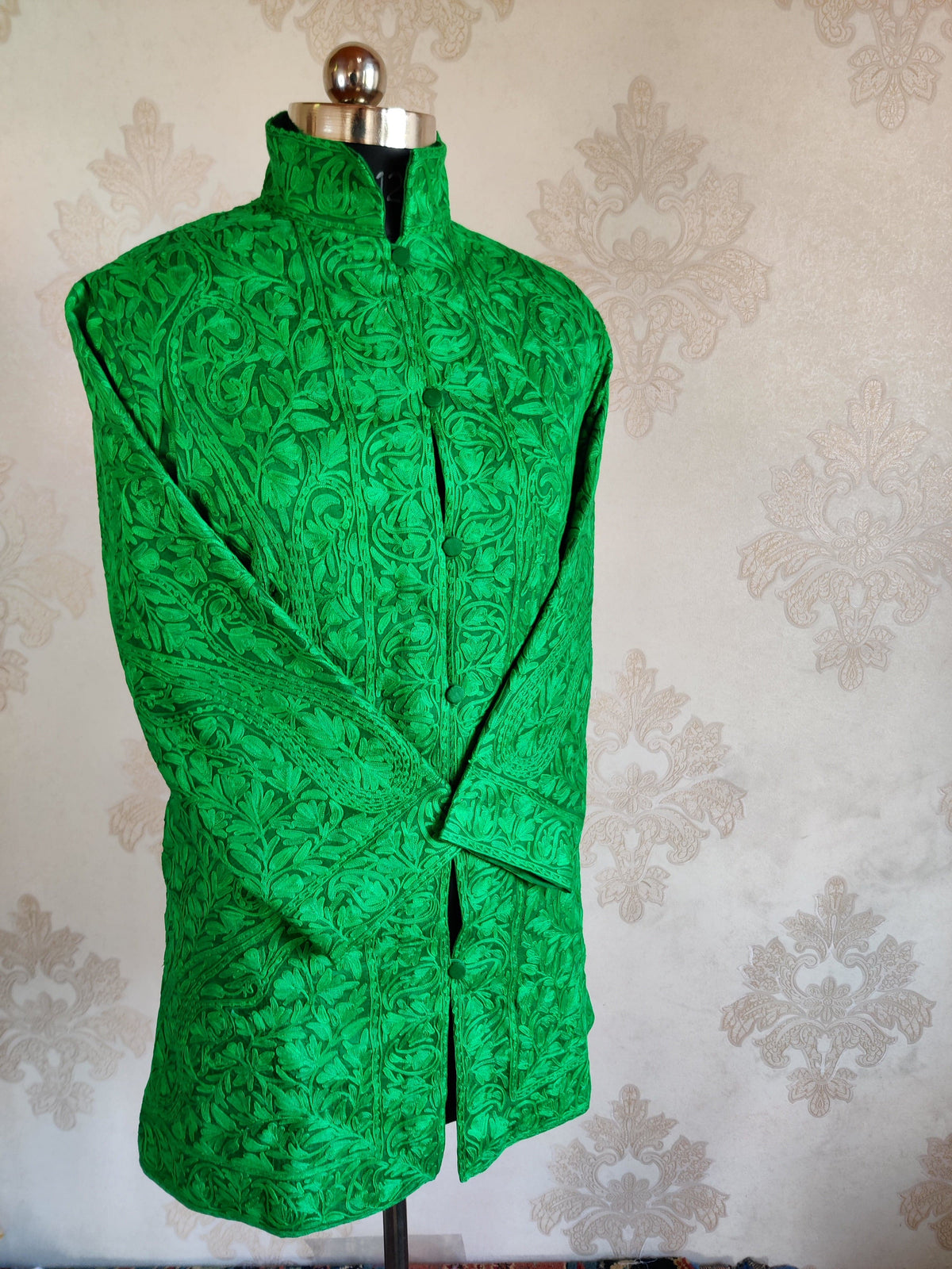 Angled front of a bright green jacket with crossed sleeves and tonal Aari paisley and floral embroidery