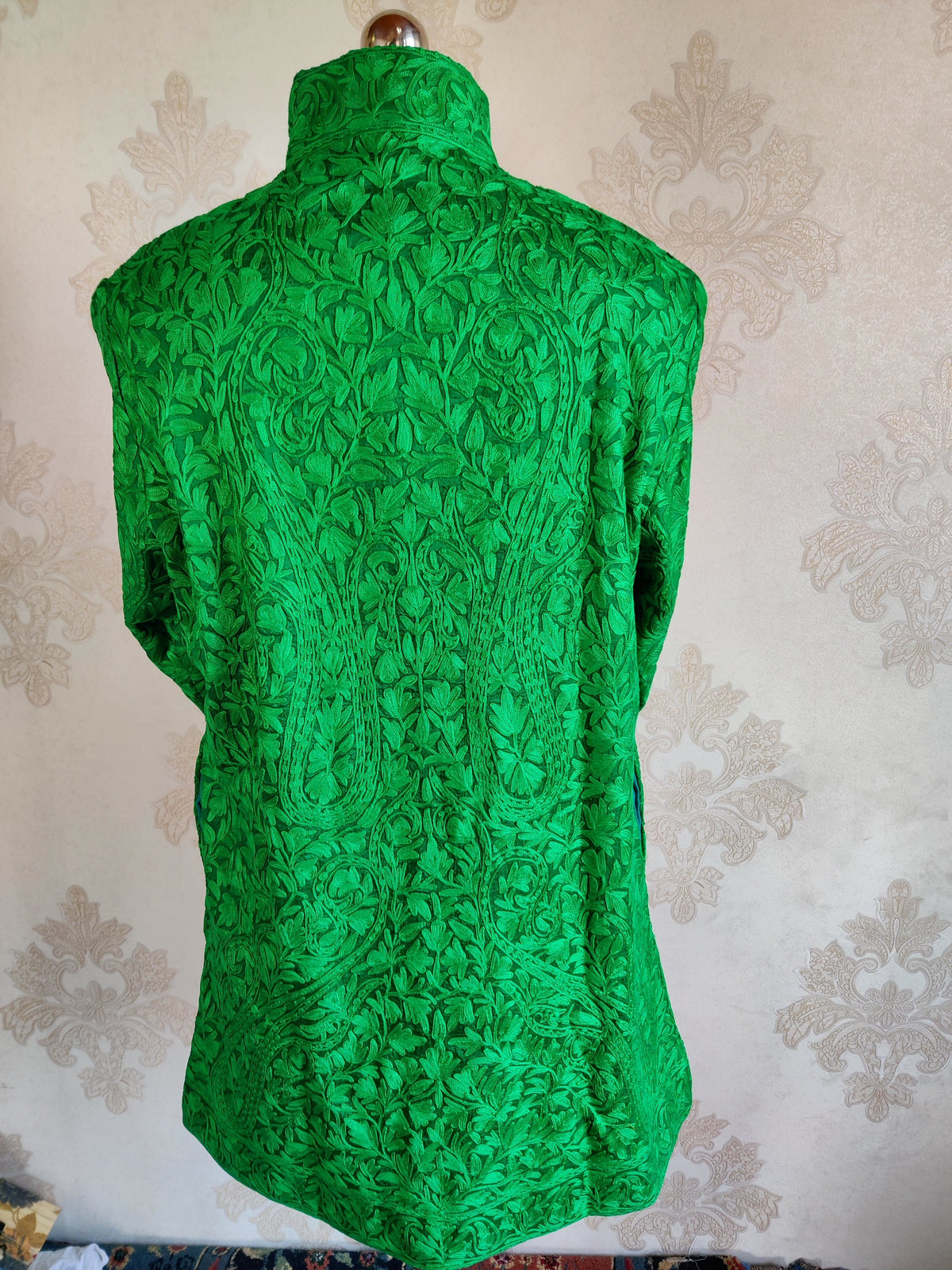 Back of a green jacket with large symmetrical tonal Aari paisleys surrounded by dense leafy vines