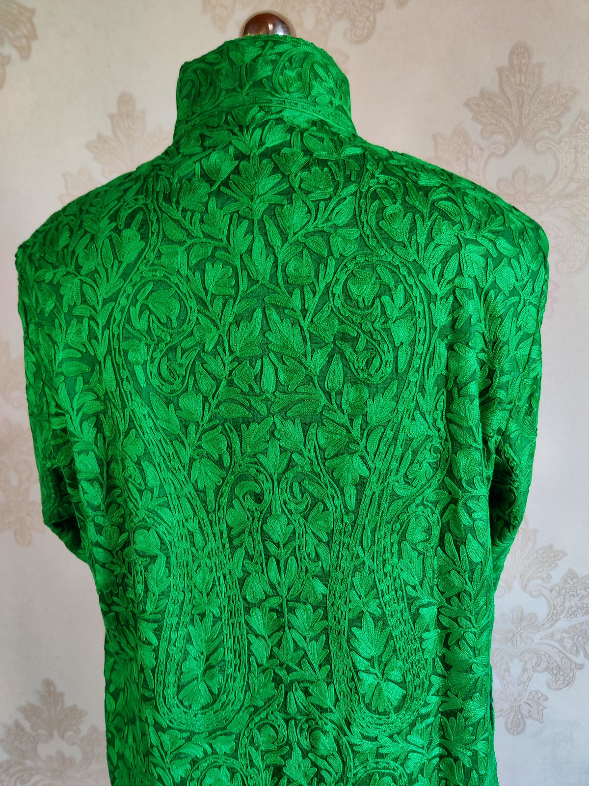 Upper back detail of a green jacket with a stand collar and large tonal Aari paisleys filled with leafy embroidery
