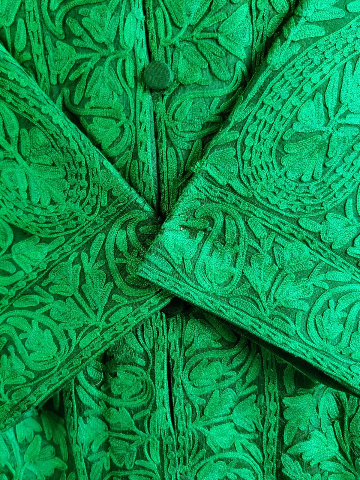 Close-up of crossed green cuffs and a covered button, surrounded by raised tonal Aari flowers and leaves