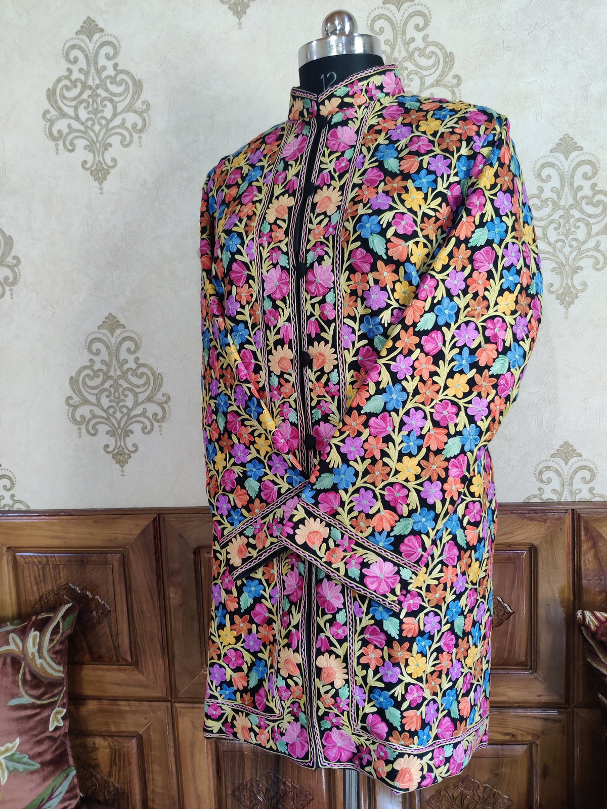 Three-quarter front of the black Aari jacket, showing all-over colourful floral vines and flower borders along the opening.