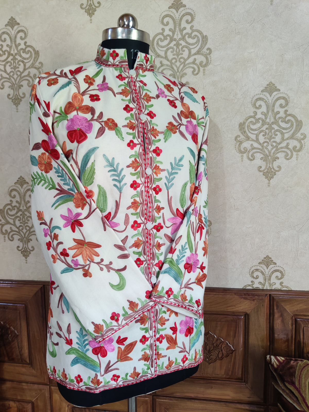 Front view of a short ivory jacket with crossed sleeves and orange, pink, red and teal floral embroidery.