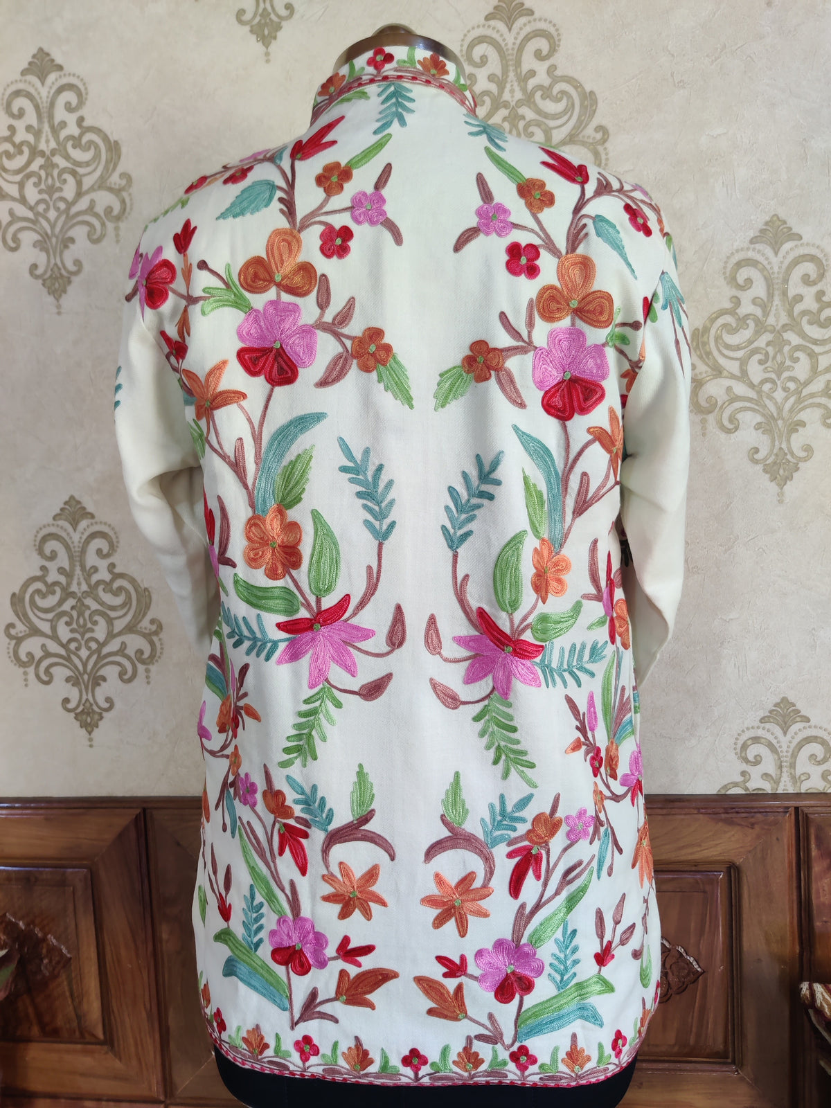 Back of a short ivory jacket with symmetrical colourful floral vines and a narrow red floral hem border.