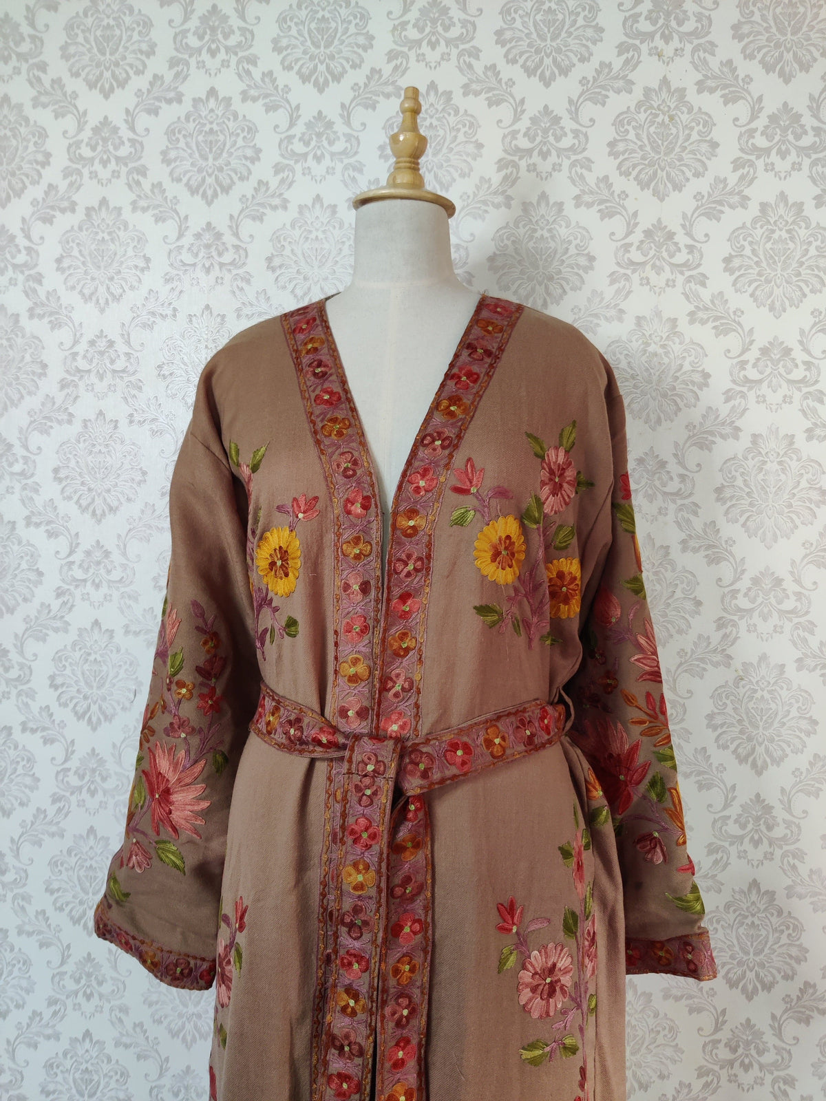 Upper front of a taupe-brown robe with a tied floral belt, pink and yellow flower motifs and wide embroidered sleeves.