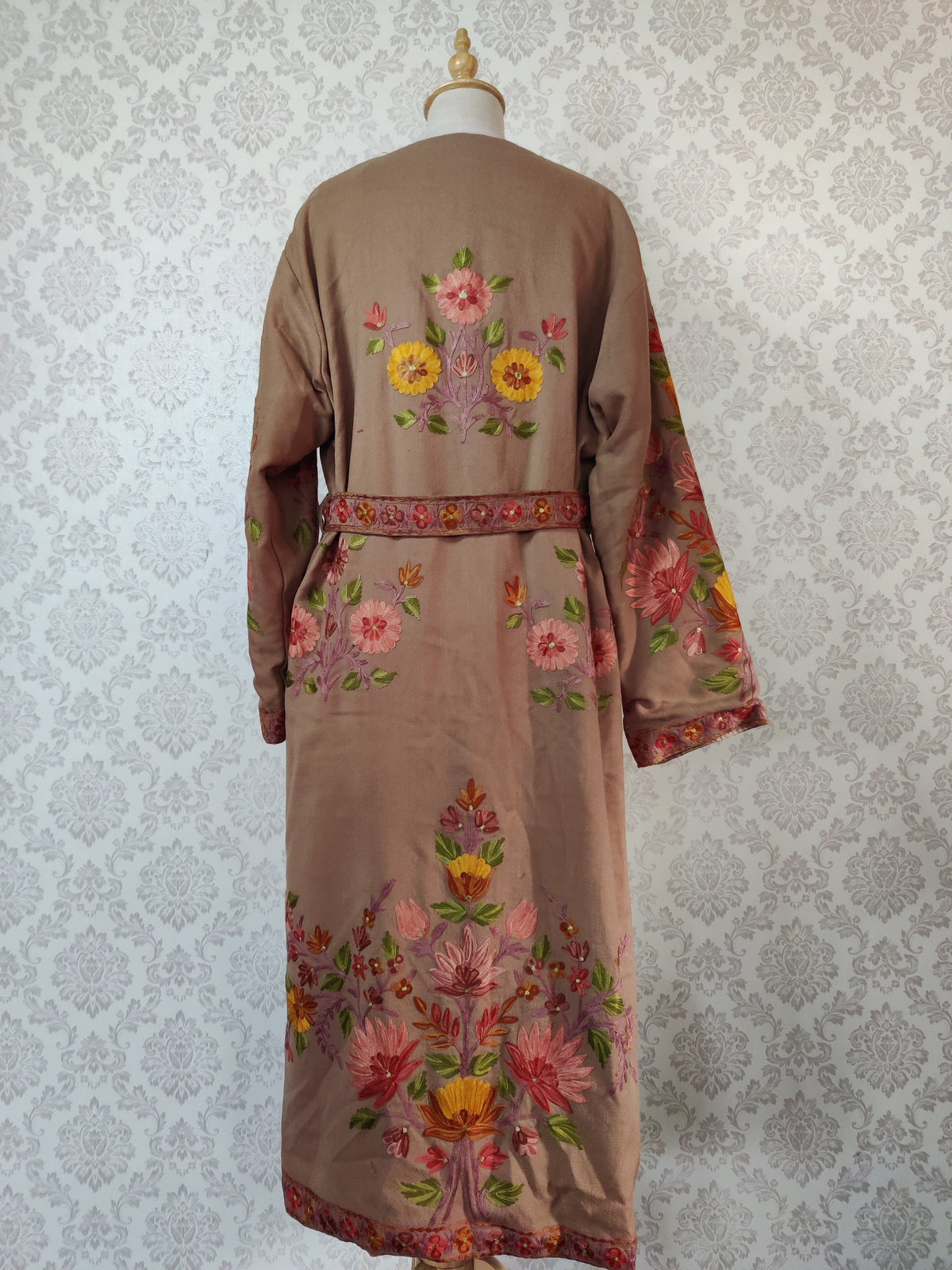 Back of a taupe-brown robe with an embroidered belt, small upper floral bouquets and a large pink and yellow arrangement near the hem.