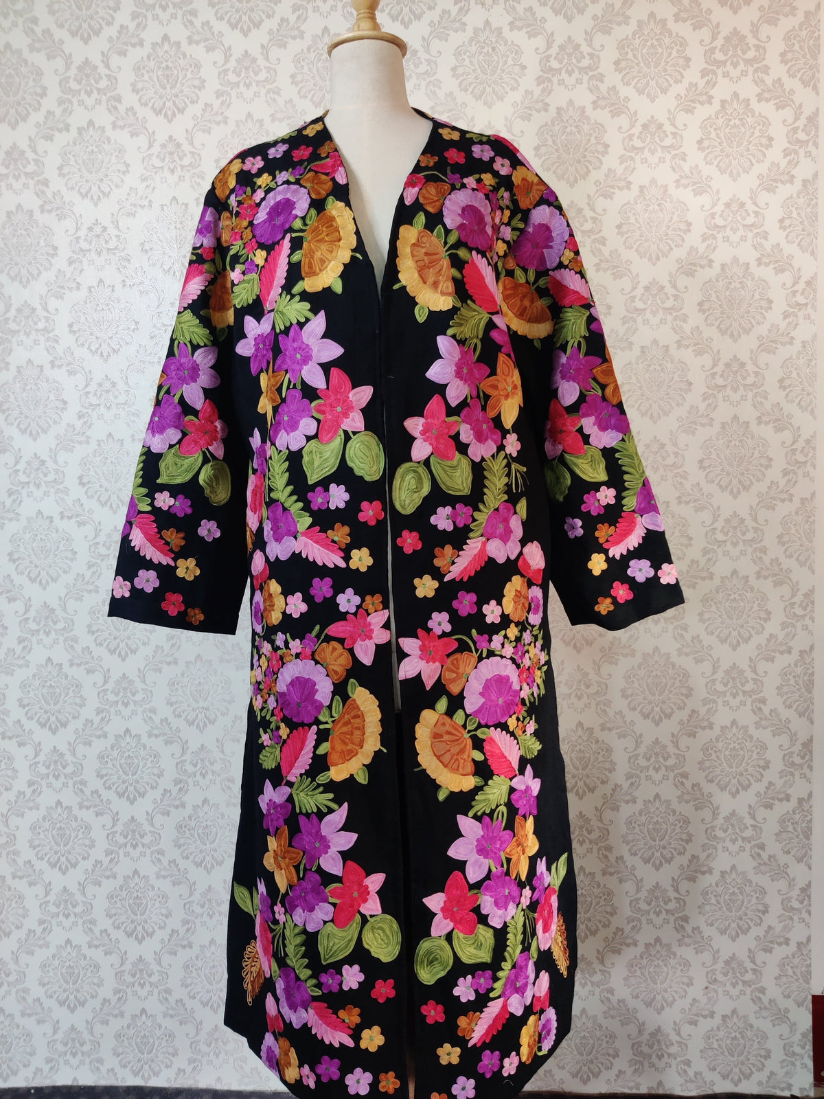 Long black robe displayed full-length on a mannequin without a belt, with colourful floral embroidery along the front and wide sleeves.