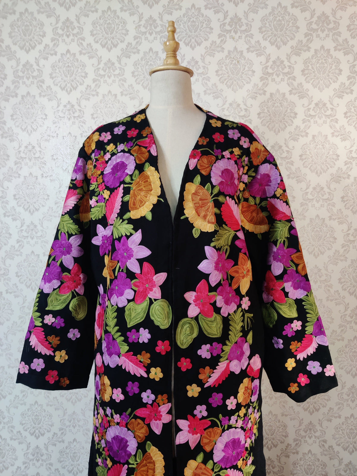 Upper view of an unbelted black robe, with large pink, purple and orange embroidered flowers, green leaves and a plain V-shaped opening.