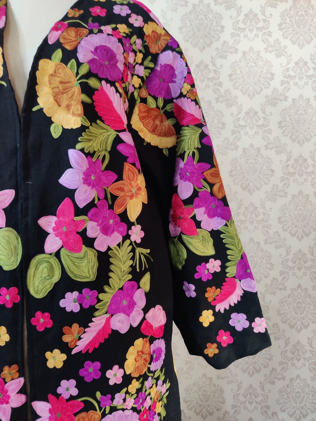 Detail of the black robe's shoulder and wide sleeve, covered with pink, purple and orange flowers and green leaves.
